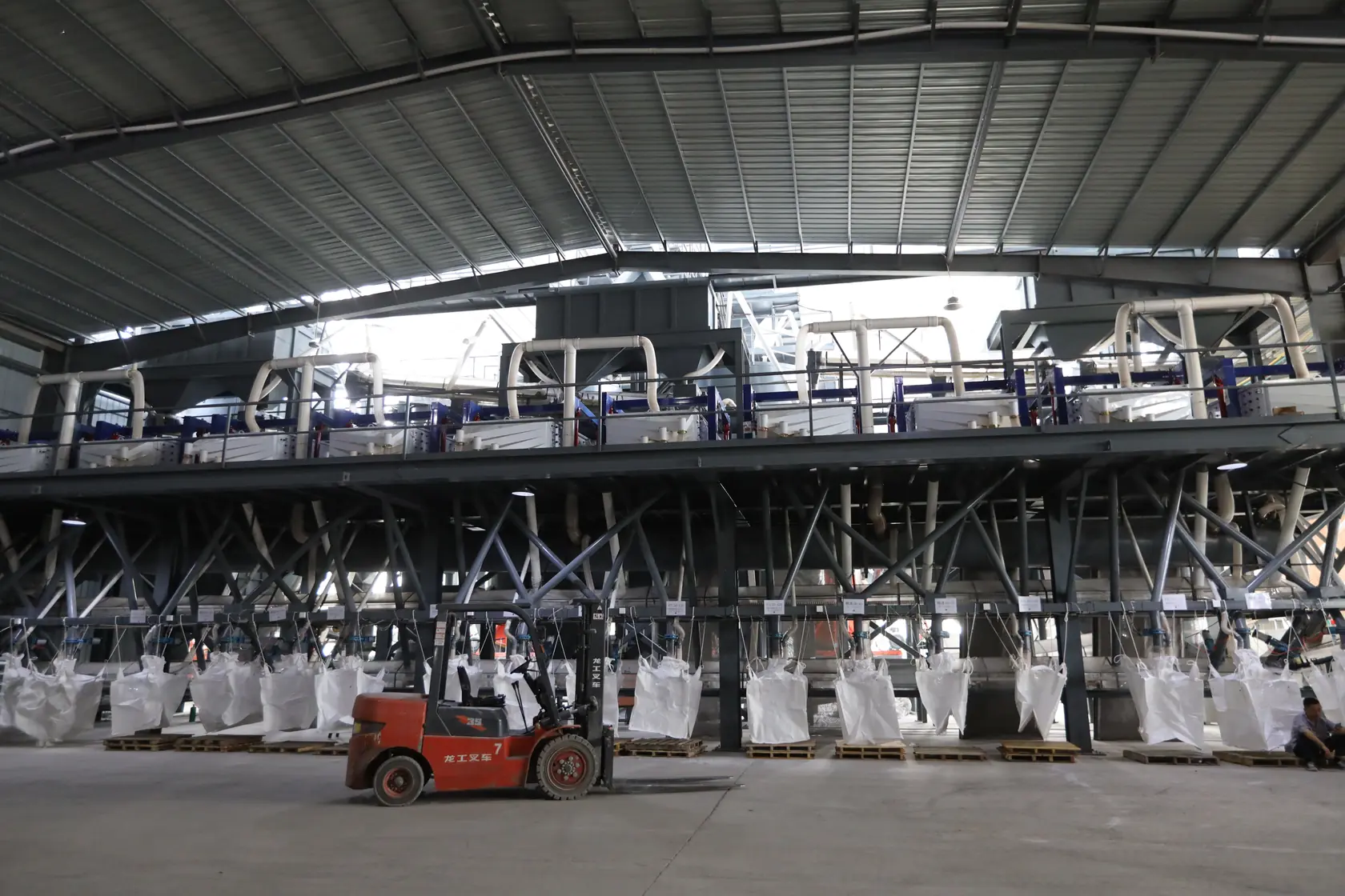 A wide workshop view with a row of bulk bags below processing equipment
