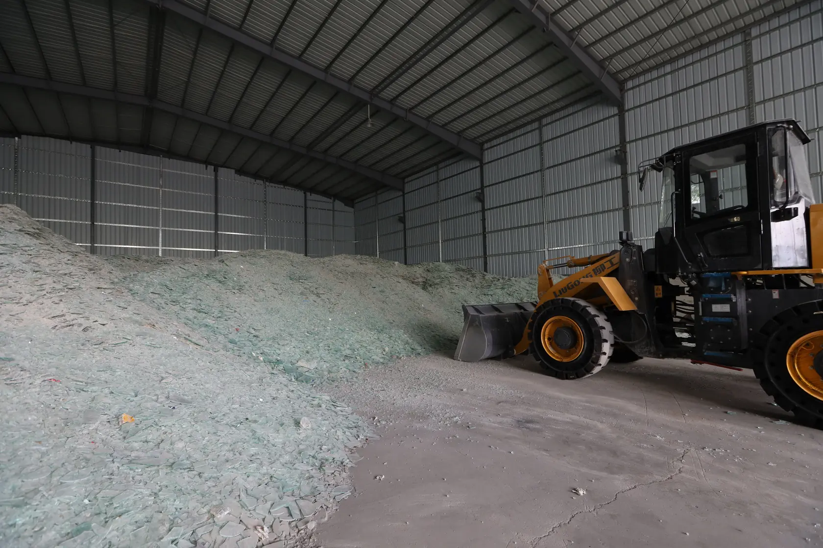 A loader beside a pile of glass fragments inside a storage building
